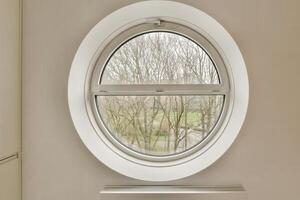 A round window in a white wall with a view of trees photo