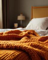 Knitted blanket in fall colors, soft and cozy, resting on the edge of a bed photo