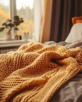 Knitted blanket in fall colors, soft and cozy, resting on the edge of a bed photo