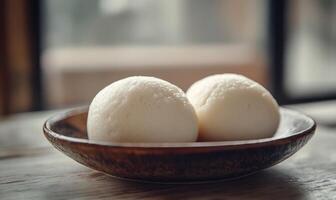 Two white pastries sit in a wooden bowl on a wooden table photo