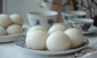 A plate of white dumplings sits on a table with a few cups and bowls photo