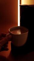 White cup with coffee, espresso machine pouring coffee with steam in backlight. Process of making coffee coming out from an automated home coffeemaker machine. High quality vertical shot video