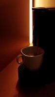 White cup with coffee, espresso machine pouring coffee with steam in backlight. Process of making coffee coming out from an automated home coffeemaker machine. High quality vertical shot video