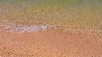 Serene beach and gentle, calm waves, yellow sand on a sunny day. Sandy beach, shore, close up top view. Horizontal 4K video