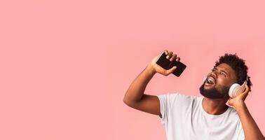 Amazing music application. Joyful black man in wireless headset listening to music and singing, using phone as mic, panorama with free space photo