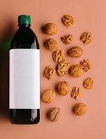 Bottle of walnut oil with walnuts scattered around on orange background photo