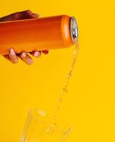 Woman pouring orange juice from can into glass on yellow background photo