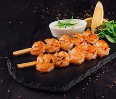 Grilled tiger prawns skewers served on stone plate with herbs and lemon photo