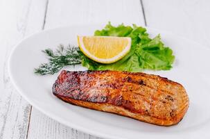 Grilled salmon steak lying on white plate with lemon and lettuce photo