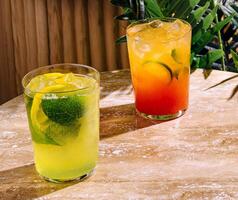 Two refreshing cocktails with lime and lemon resting on table in the sun photo