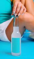 Woman opening bottle of refreshing cold drink with blank label on blue background photo