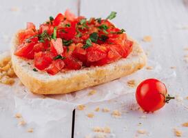 Delicious bruschetta with chopped tomatoes and basil resting on paper on white table photo