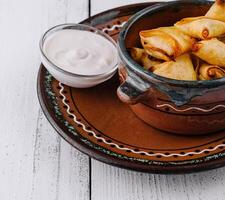 Small baked pies are lying in a ceramic bowl on a white wooden table photo