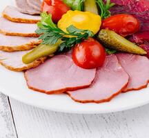 Plate combining several types of meat cuts and pickles being served on white table photo