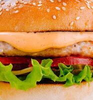 Delicious burger with chicken patty, fresh vegetables and sauce on a sesame seed bun photo