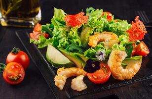 Fresh salad with shrimps, avocado and cherry tomatoes on black wooden table photo
