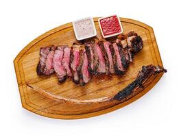 Grilled tomahawk steak lying on wooden board with sauces photo