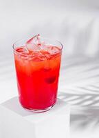 Red cocktail standing on white cube with palm leaf shadow photo