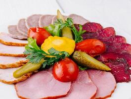 Plate combining several types of meat cuts and pickles being served on white table photo