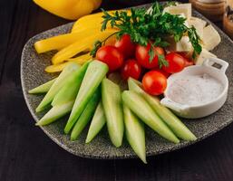 Plate presenting sliced cucumbers, tomatoes, cheese and peppers with spices aside photo