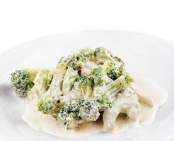 Steamed broccoli florets covered with creamy cheese sauce on white plate photo