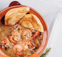 Creamy shrimp stew served in a terracotta bowl with toasted bread and herbs photo
