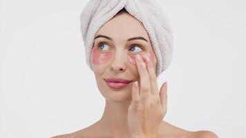 Close-up of a young woman with under-eye patches targeting wrinkles and dark circles. Isolated against a white background, this image emphasizes skincare and the fight against signs of fatigue video