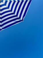 Fragment of white and blue striped beach umbrella close up against clear blue sky with text space photo
