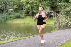 Active Senior Woman Jogging Outdoors in a Park with a Lake and Trees in the Background photo