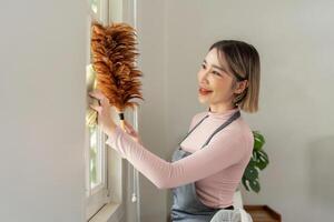 Housekeeper dusting window with feather duster in living room photo