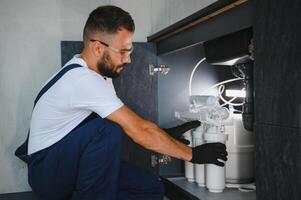 Plumber installs or change water filter. Replacement aqua filter. Repairman installing water filter cartridges in a kitchen. Installation of reverse osmosis water purification system photo