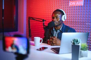 african american vlogger using smartphone to film podcast in studio. blogger with mobile phone, microphone and headphones filming photo