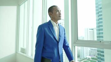A businessman in a blue suit stands by a large office window, looking out at the city skyline while holding a laptop. The scene suggests reflection, ambition, and strategic thinking. video