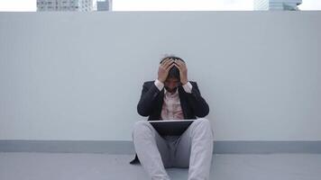 A businessman in formal attire sits on the ground with his head in his hands, conveying frustration or stress. The isolated setting highlights personal or professional challenges. video