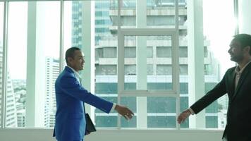 Two businessmen shake hands in an office setting with large windows and a city view. The handshake signifies agreement, partnership, or the conclusion of a successful meeting. video