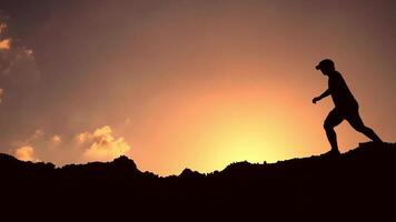 Silhouette of a man walking on a mountain at sunset video