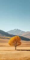 Vibrant autumn grassland with a lone tree and majestic mountains nearby photo
