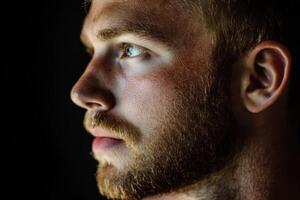 Close-up of a young man with a beard gazing thoughtfully in low light photo