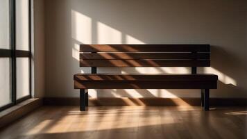 A simple brown bench sits in a room with sunlight streaming through the window, casting long shadows on the wall. photo