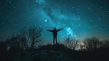 A lone figure standing on a hilltop, their arms outstretched towards the stars, as if reaching for the secrets of the universe. photo