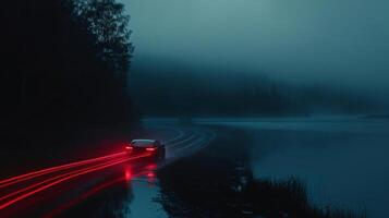 The camera pans over to a lone car making its way around the lake its taillights leaving a trail of red on the dark road. The stillness of the night adds a sense of calm an photo