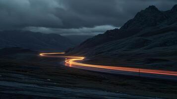A solitary car making its way along the mountain road with the headlights creating a trail of light in the darkness photo