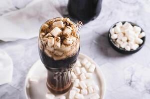 Refreshing fluffy coke with marshmallow in a glass on the table photo