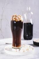 Trendy drink of cola and marshmallow in a glass on the table vertical view photo