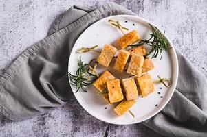 Close up of spicy fried tofu on skewers and rosemary on a plate on the table top view photo