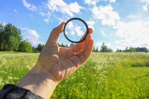 Hand holds a circular polarizer filter on summer landscape background. photo
