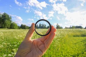Hand holds a circular polarizer filter on summer landscape background. photo
