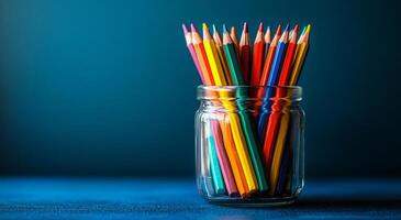 A jar full of colored pencils on a blue background. The pencils are of different colors and are arranged in a neat manner. The jar is placed on a table photo
