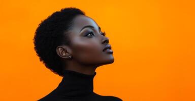 A woman with a short haircut and a black sweater is looking at the camera. The orange background adds a warm and inviting atmosphere to the image photo