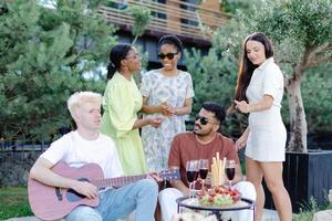 Multicultural group of people, man playing guitar and friends dancing, singing and having fun photo